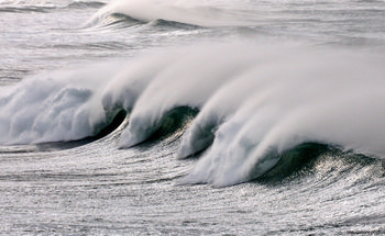 Rolling waves This landscape photograph, captured along the coast of the United Kingdom, depicts rolling waves in the late morning during the winter season. The image highlights the power and movement of nature as large waves break in succession, creating a misty spray that drifts across the surface of the water. The lighting and conditions, characteristic of winter, give the ocean a silvery, textured appearance, emphasizing the dynamic patterns created by the waves. This photograph showcases the raw beauty of coastal nature in the United Kingdom, focusing on the impressive form and energy of the waves.